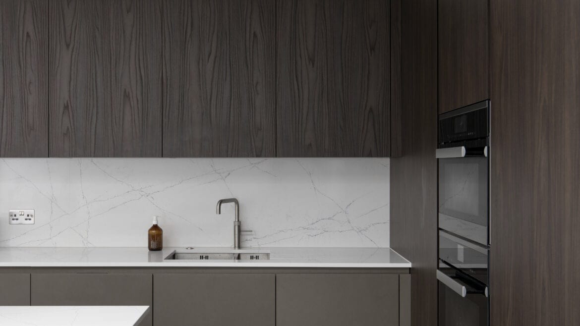 Modern kitchen with dark wood cabinets, white countertop, stainless steel faucet, and built-in oven.