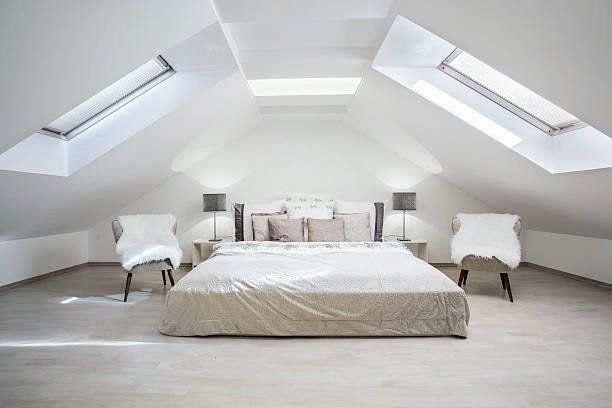 Bright attic bedroom with skylights, bed, two chairs, and two lamps.