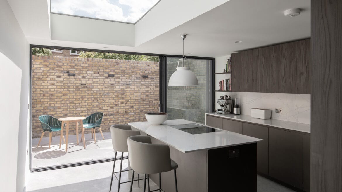 Modern kitchen with island, barstools, and sliding glass doors opening to a patio with brick wall.