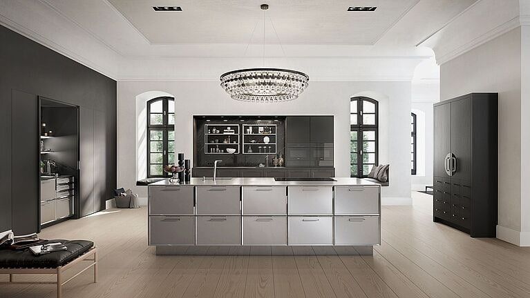 Modern kitchen with stainless steel island, dark cabinetry, and chandelier.
