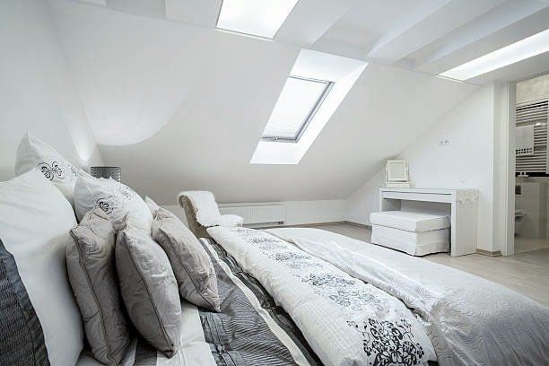 White bedroom with skylights, a bed with pillows, and a small vanity.