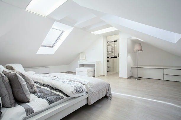 Bright white bedroom with slanted ceiling, skylights, and bed.  A dressing area and built-in storage are also visible.