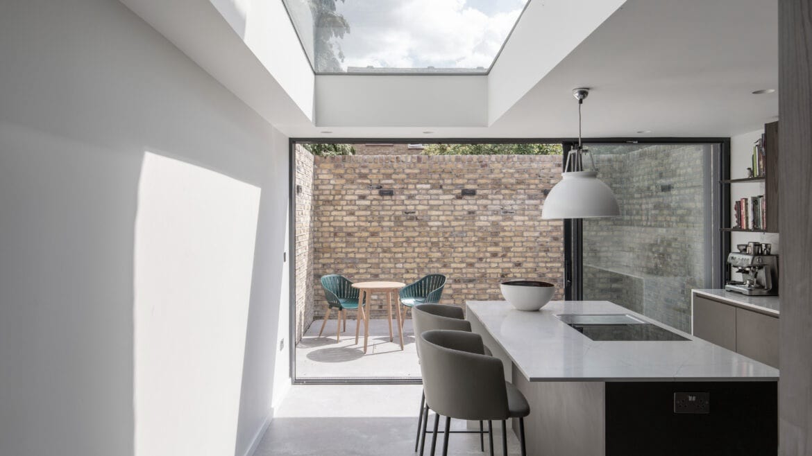 Modern kitchen with skylight and island, looking out to a patio with brick wall and chairs.
