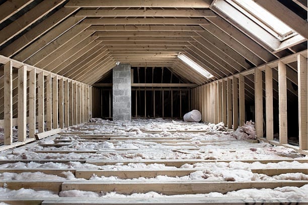 Unfinished attic with wooden frame, insulation, and chimney; skylight overhead.