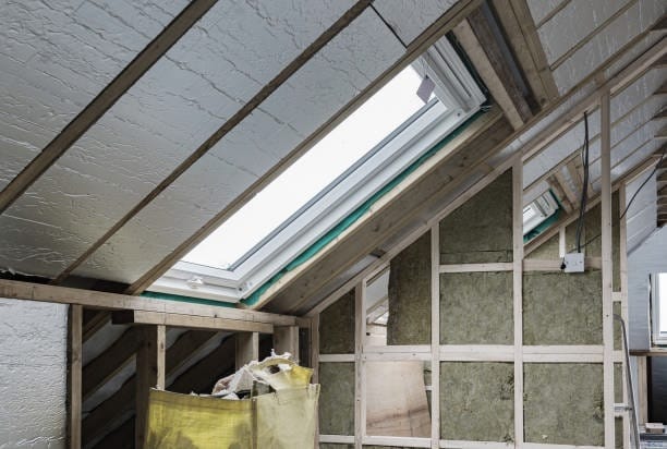 Attic interior with skylight, wood framing, insulation, and reflective material.