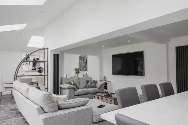 Modern open-plan living space with a large sofa, dining area, and television on the wall.