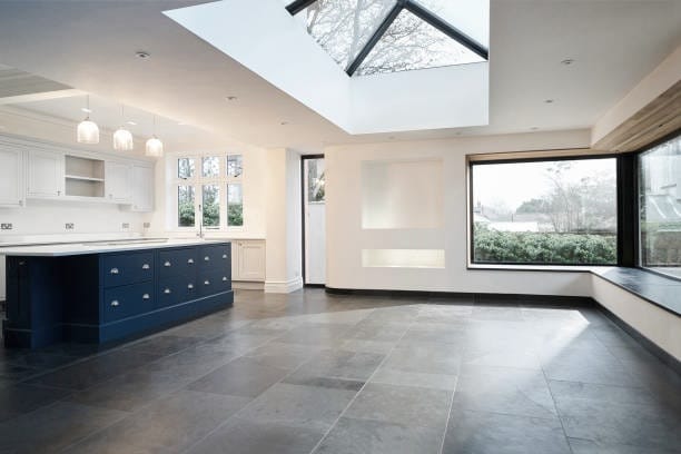 Spacious kitchen with blue island, large window, skylight, and dark gray floor. White walls, light fixtures.
