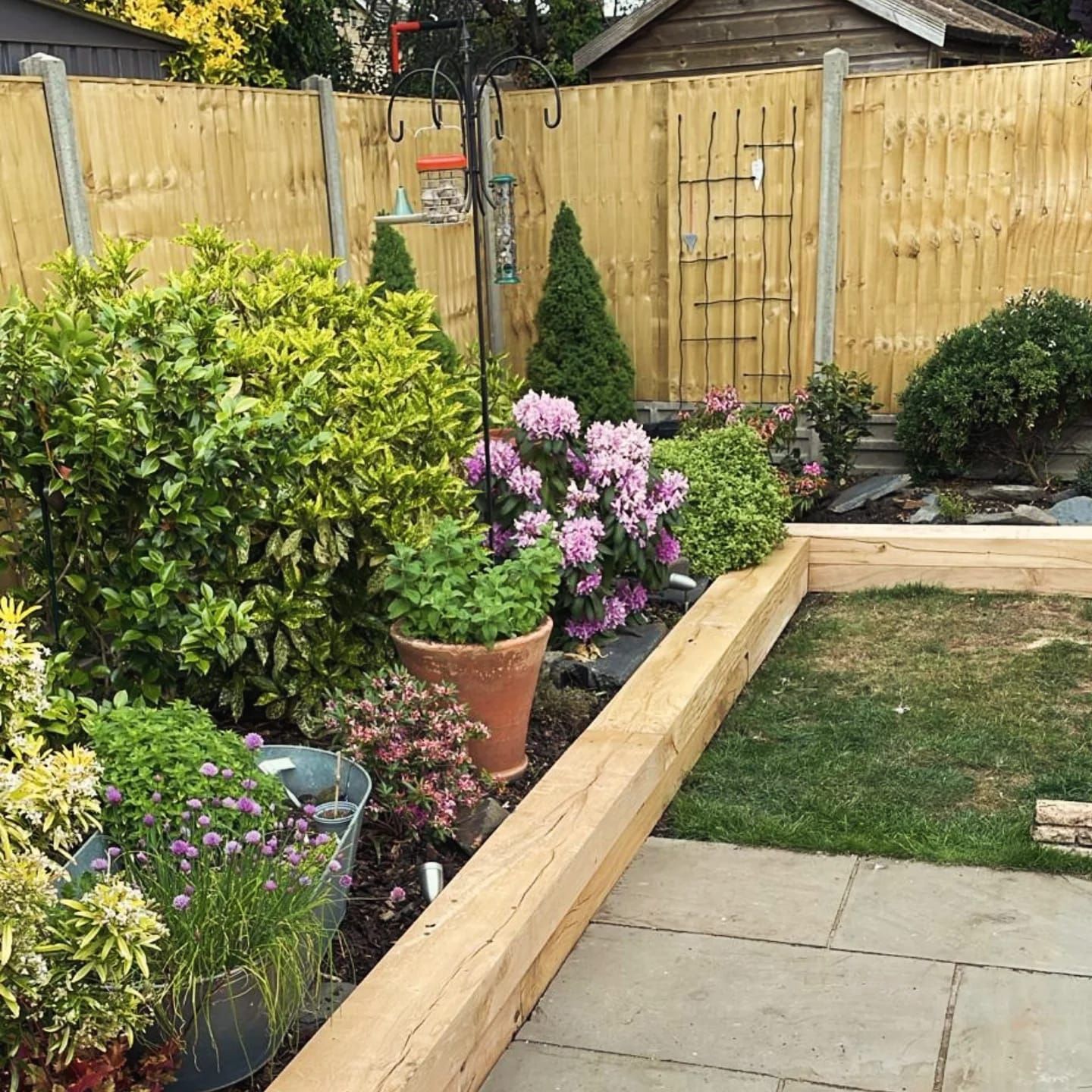 Well-kept garden with wooden fence, raised flower beds, lush greenery, and a bird feeder.