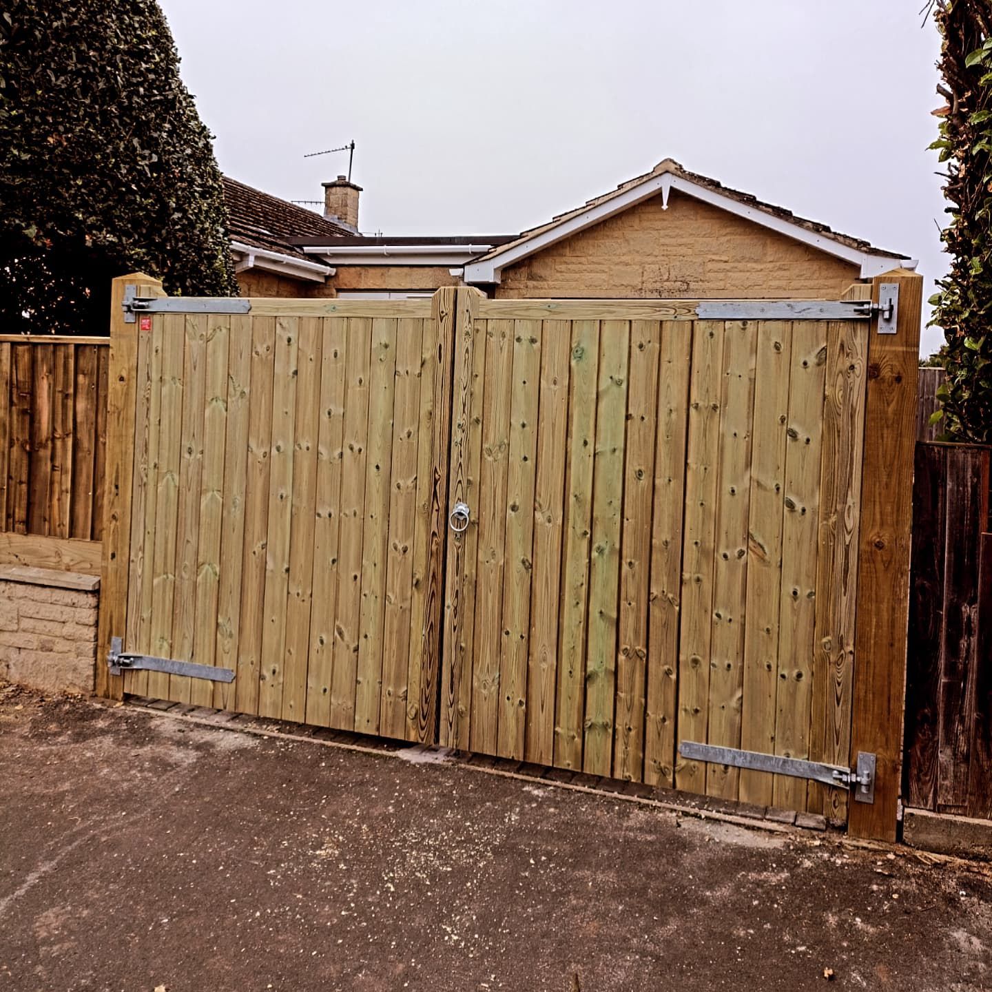 Wooden double gates with metal hinges, closed, in front of a house.