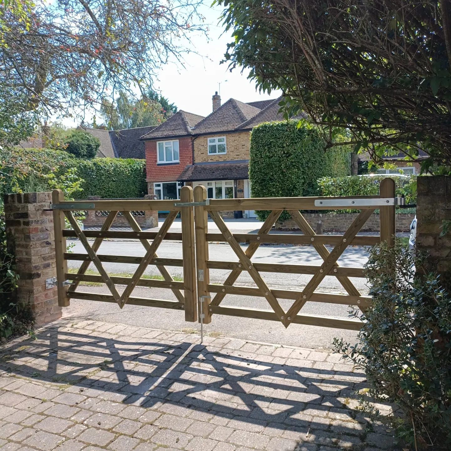 Wooden gate with star-shaped accents, leading to a brick driveway and a house with a red and beige facade.