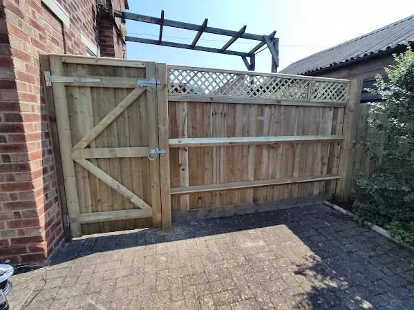 Wooden gate and fence section next to a brick wall, with a lattice top, and paving.