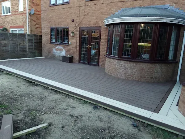 Brown composite deck beside a brick house with a bay window and double doors.