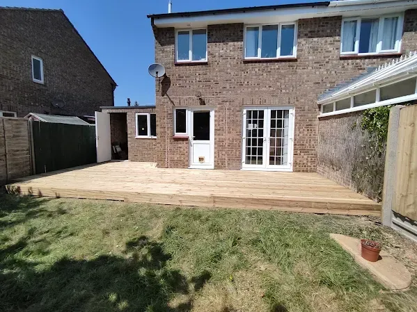 Backyard with wooden deck, brick house, shed, and green lawn on a sunny day.
