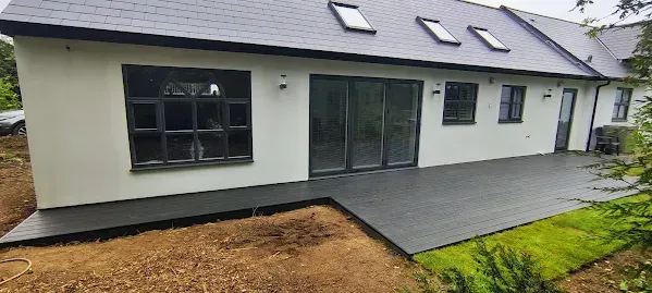 Exterior of a house with a dark gray deck. Beige walls, dark-framed windows, and a gray roof.