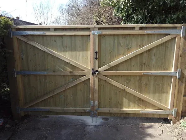 Wooden double gate with diagonal braces, metal hardware, and a handle.