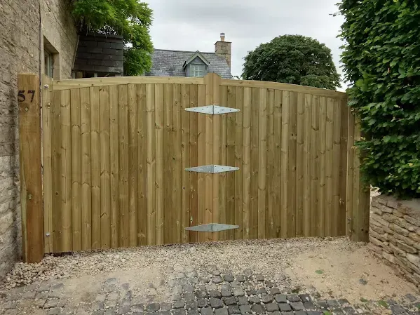 Wooden gate in a stone-walled entrance with the number 57. Gravel driveway with cobblestone path.