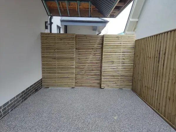 Wooden slat fences enclosing a gravel-covered outdoor space, partially sheltered by a roof.