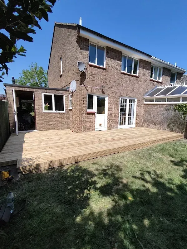 Backyard with a two-story brick house, shed, wooden deck, and green lawn on a sunny day.