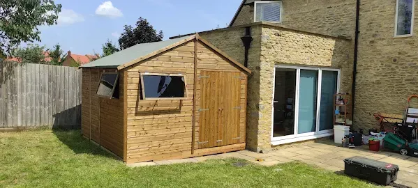 A wooden shed next to a house with sliding glass doors on a sunny day.