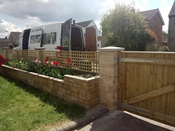 Wooden gate and fence with lattice, brick planter with tulips, van in background.