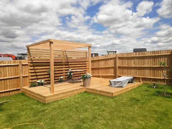 Wooden deck with pergola and bench in a backyard with a wooden fence and green grass.