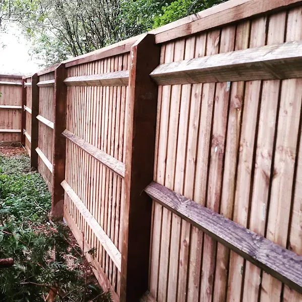 Wooden fence in a garden, with vertical planks and horizontal supports, brown color.