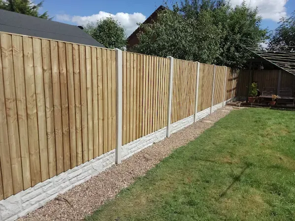 Wooden fence with concrete posts and gravel border in a yard with grass.
