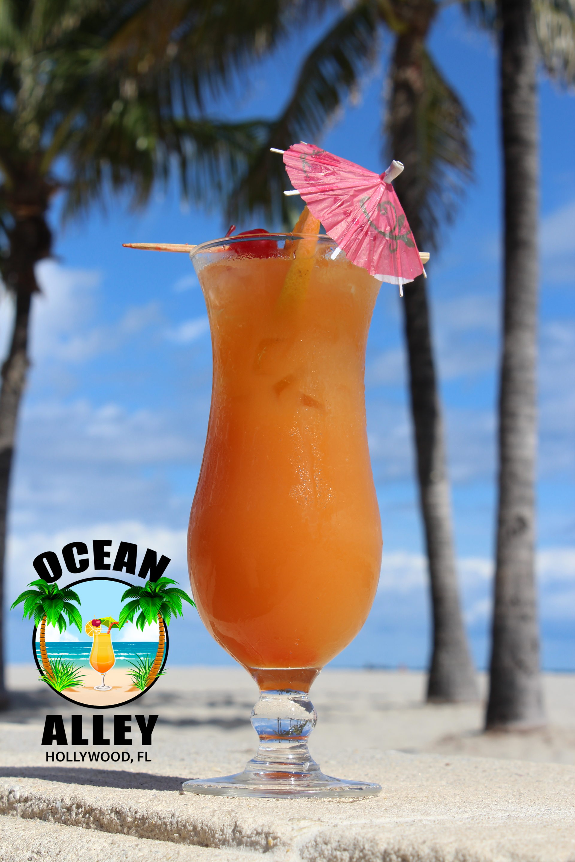 A glass of orange juice with a pink umbrella on a beach.
