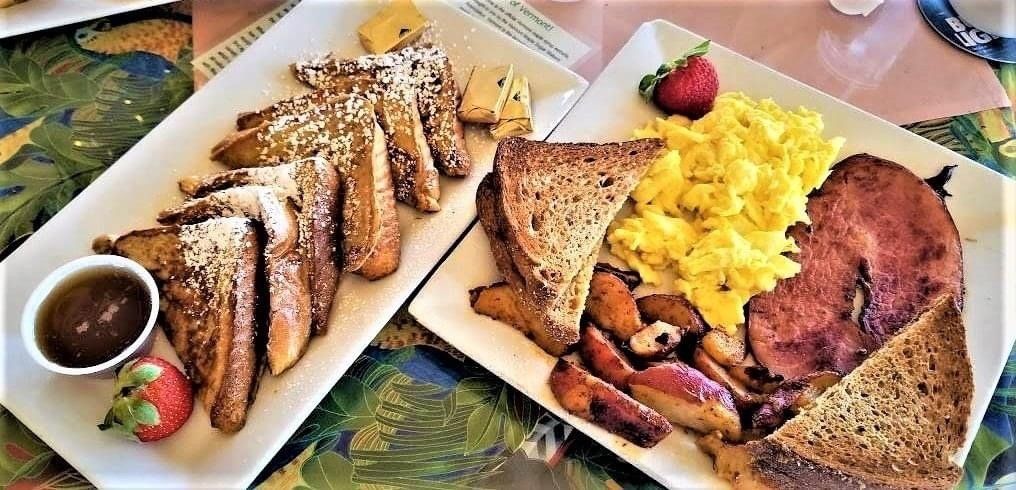 There are two plates of food on the table , one of which is french toast.