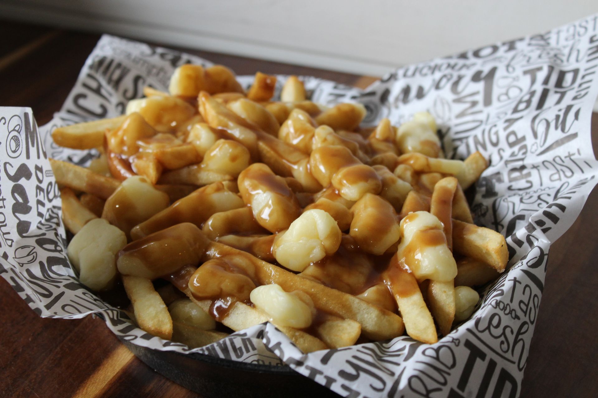A bowl of poutine is sitting on a wooden table.