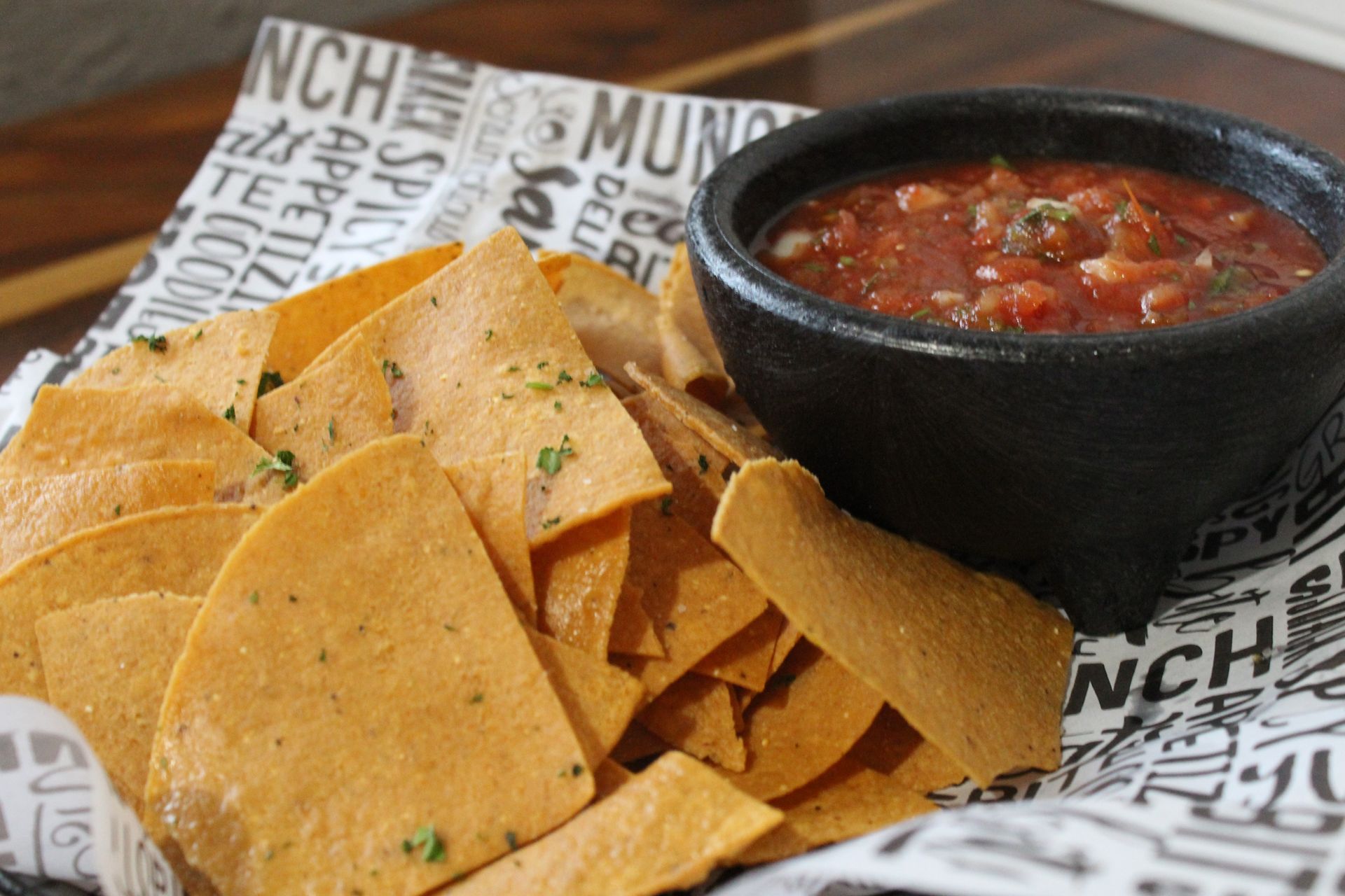 A bowl of salsa sits next to a basket of tortilla chips