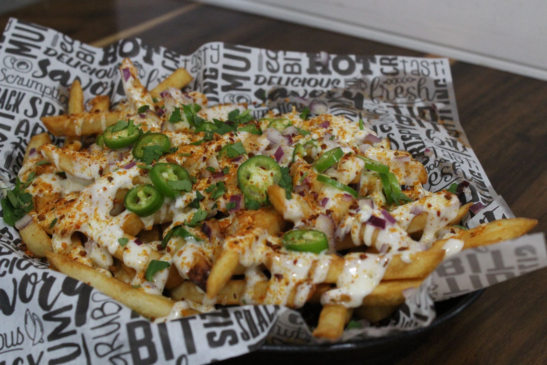 A plate of french fries with jalapenos and cheese on a table.