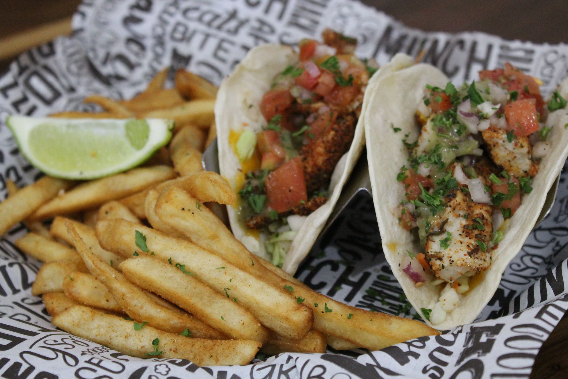 A basket of tacos and french fries on a table.