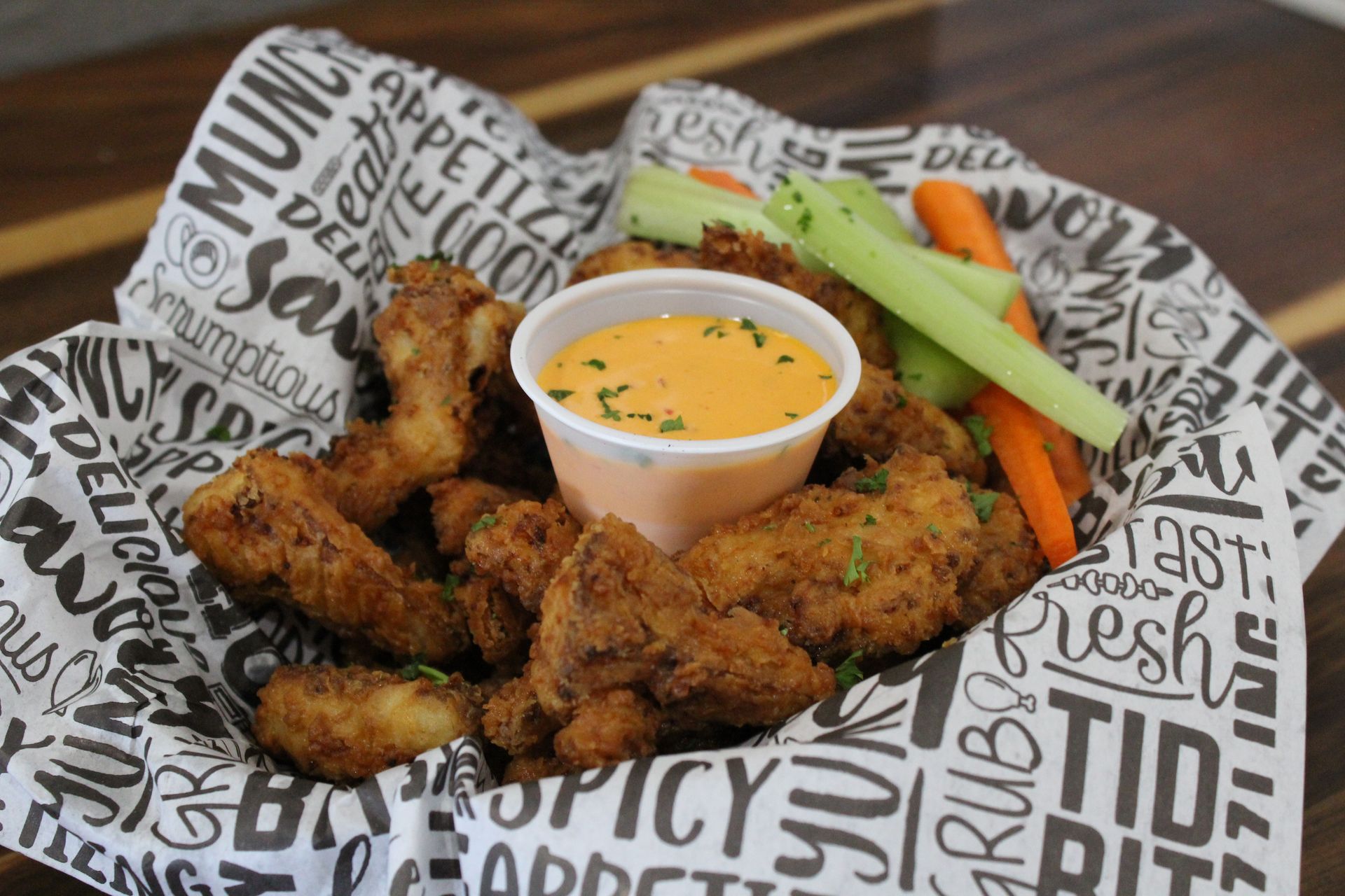 A basket of chicken wings and vegetables with a dipping sauce