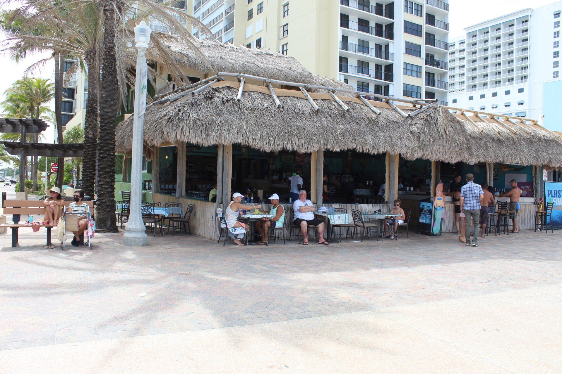 A group of people are sitting outside of a restaurant with a thatched roof