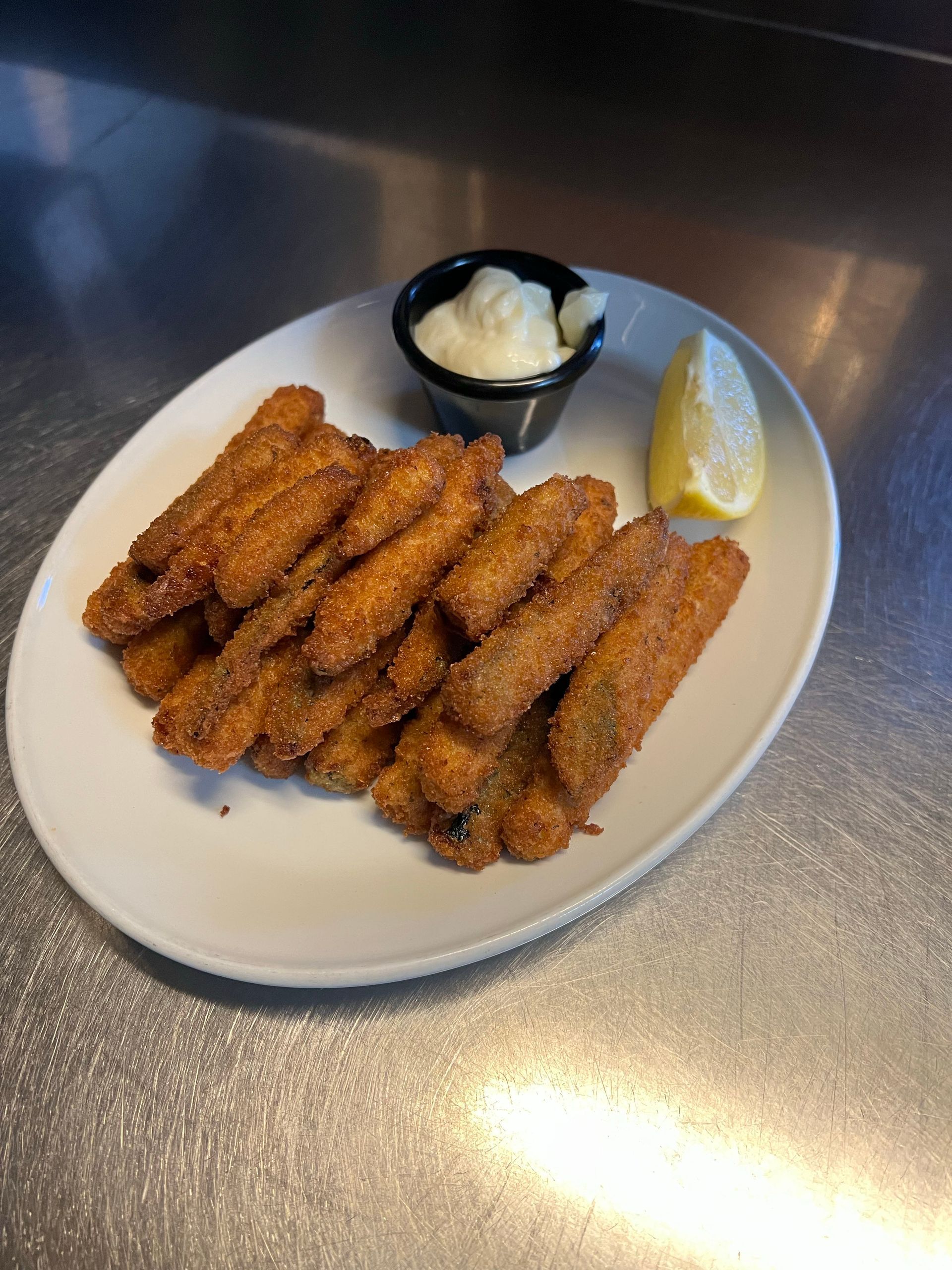 Pile of fried food, dipping sauce, and lemon wedge on a white oval plate, on a shiny surface.