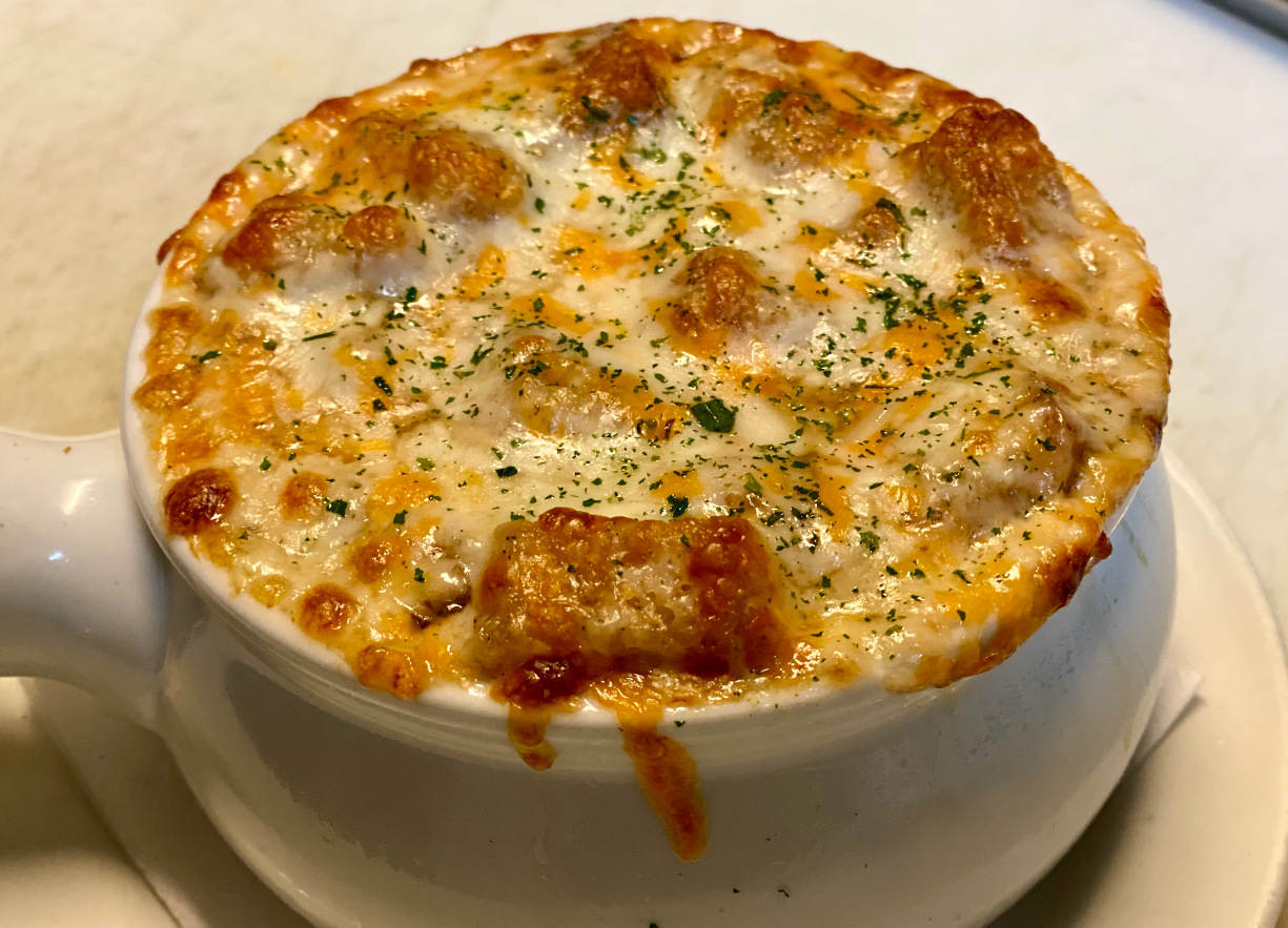 French onion soup in a white bowl, topped with melted cheese and toasted bread.
