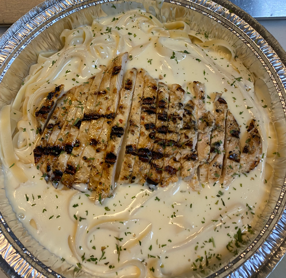 Fettuccine Alfredo with grilled chicken in a foil container, garnished with parsley.