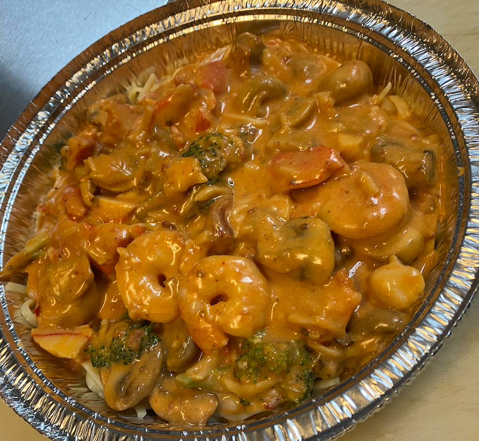 Shrimp and vegetables in creamy orange sauce, served over rice in a foil container.