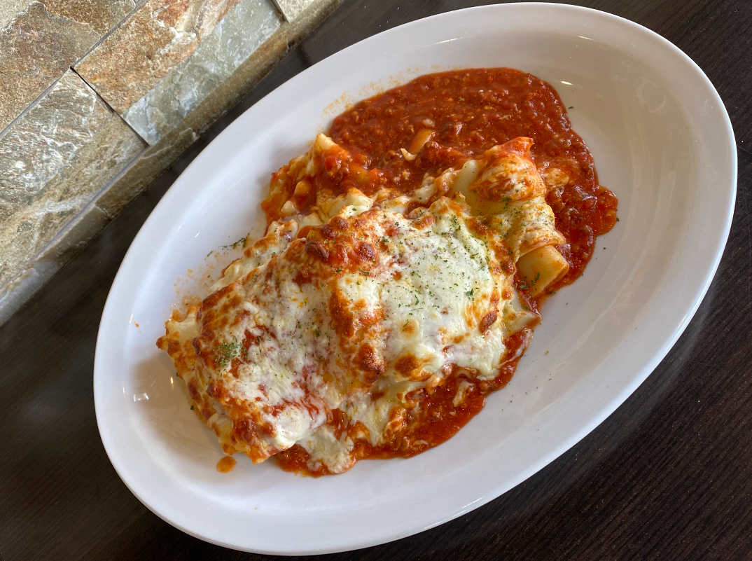 Lasagna covered in melted cheese and red sauce, served on a white oval plate.
