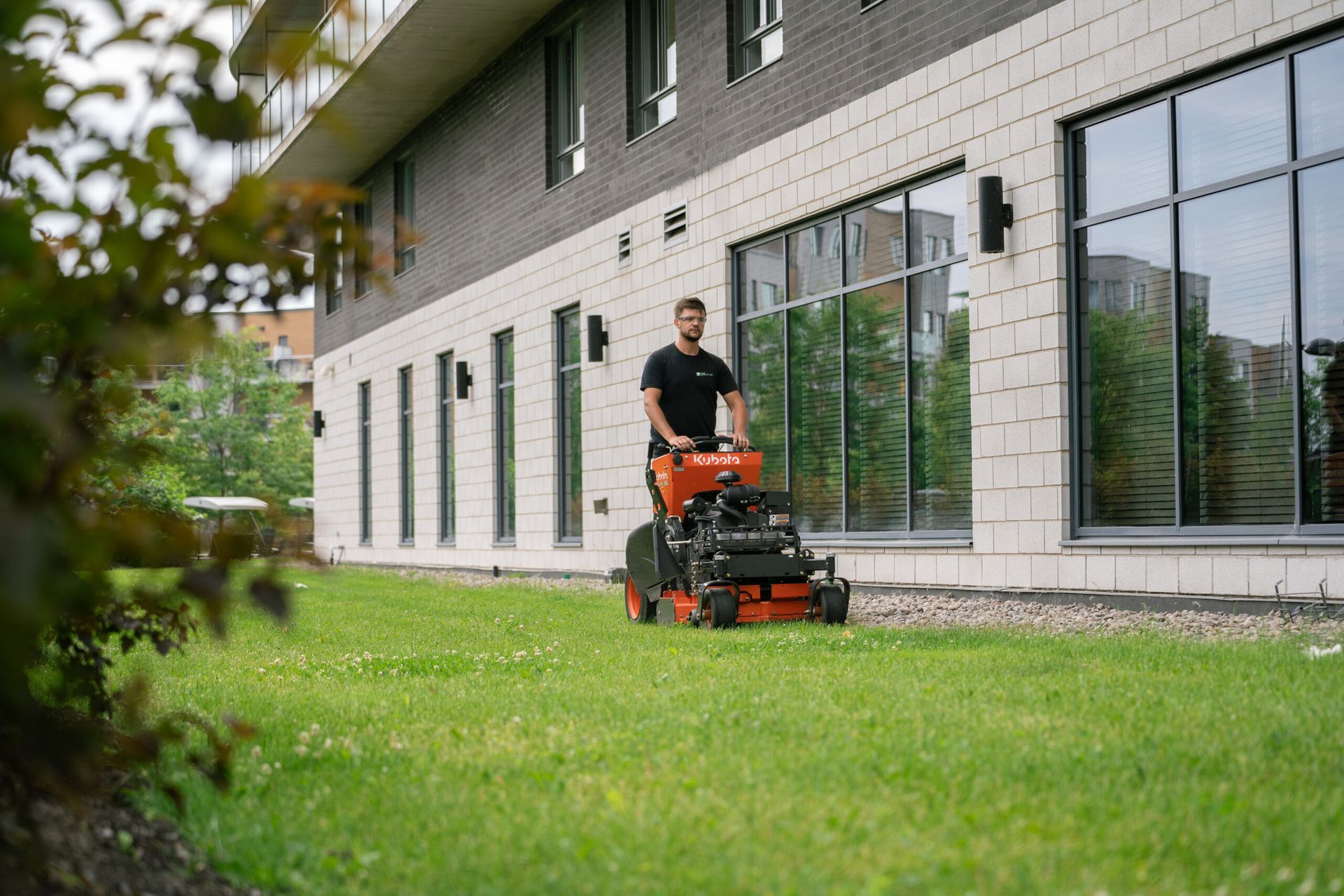 Un homme conduit une tondeuse à gazon sur une pelouse verte luxuriante devant un bâtiment.