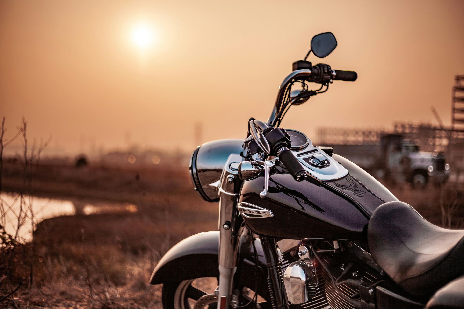 Motorcycle parked at sunset on a rural road, with warm orange sky and fields in the background