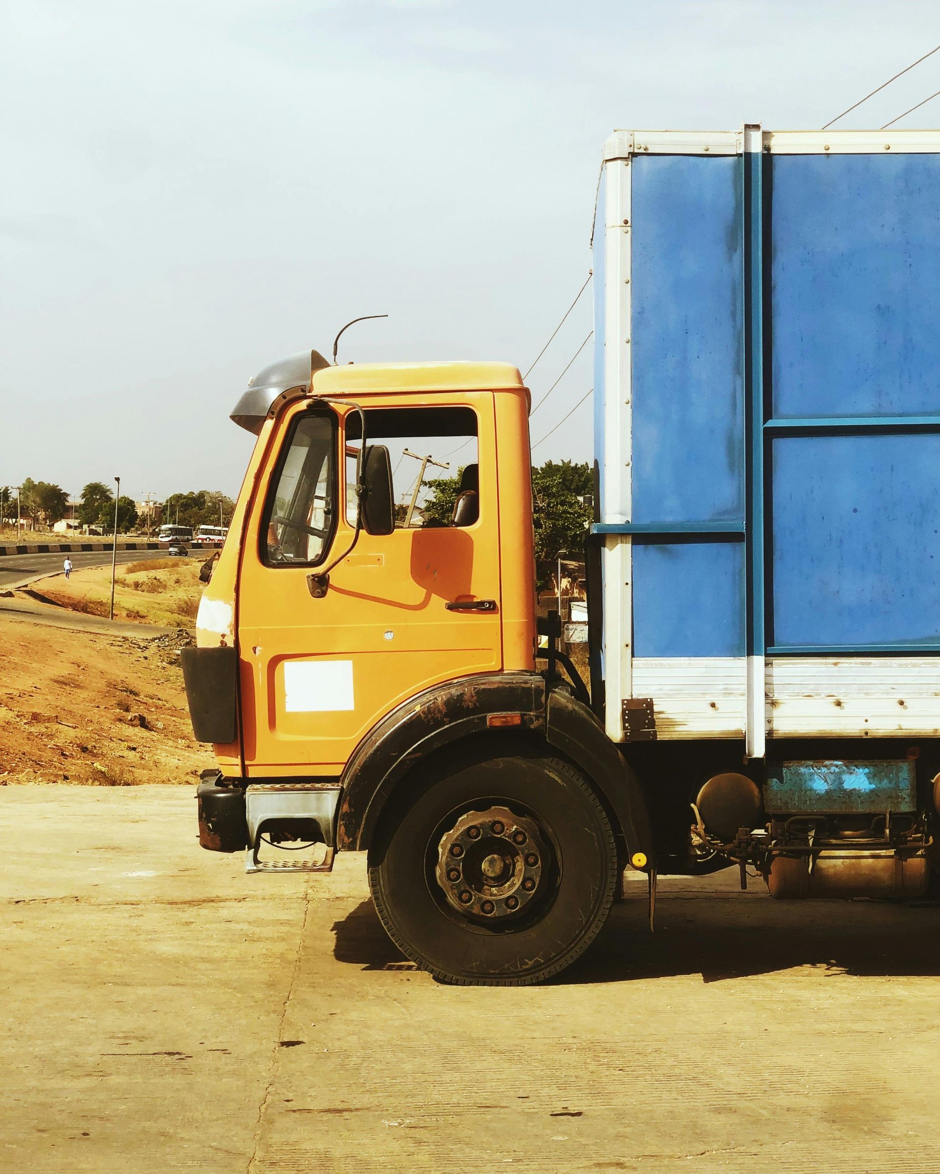 Yellow truck with blue cargo container on a dirt road outdoors
