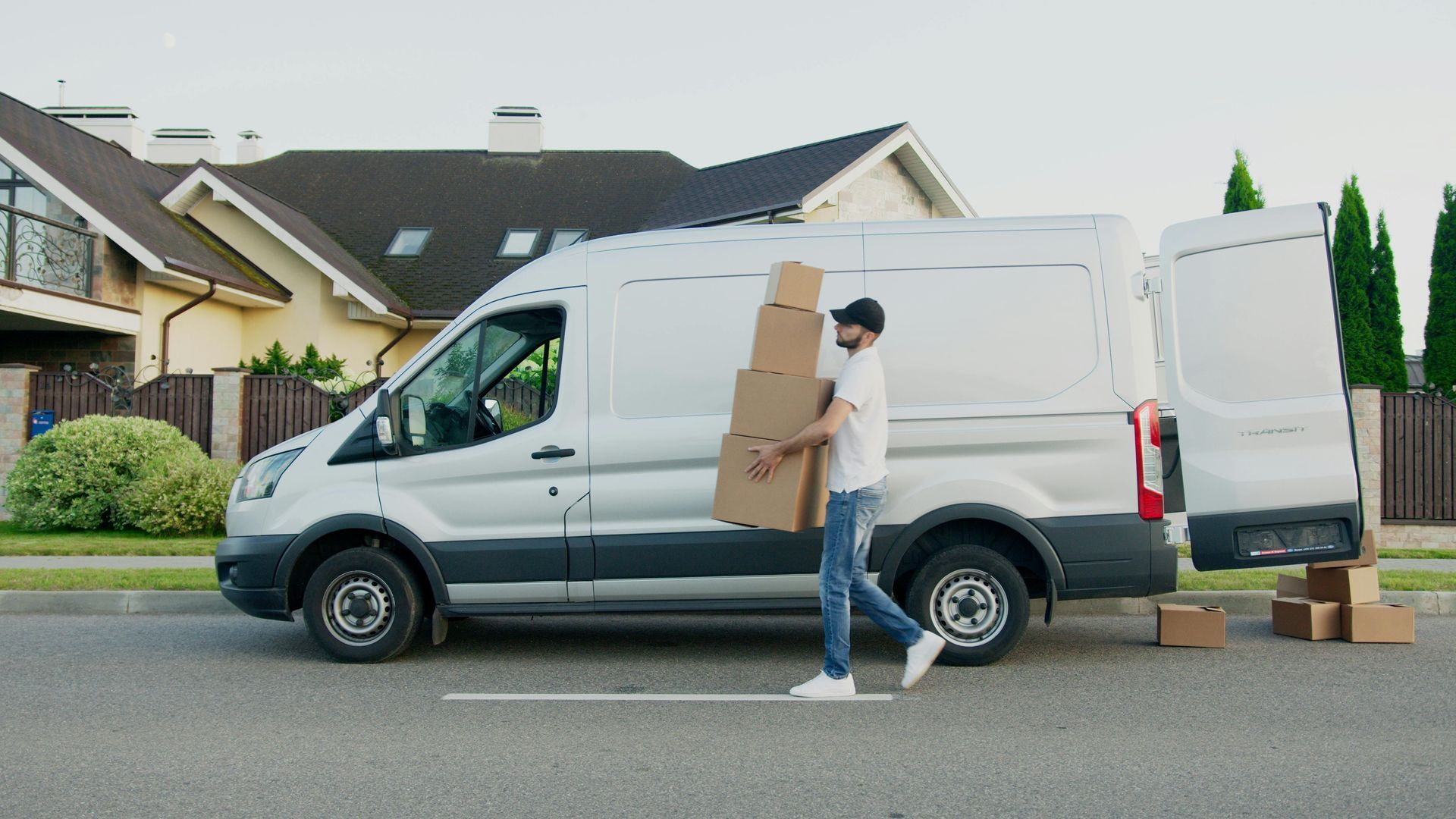 Person carrying boxes beside a white delivery van on a suburban street
