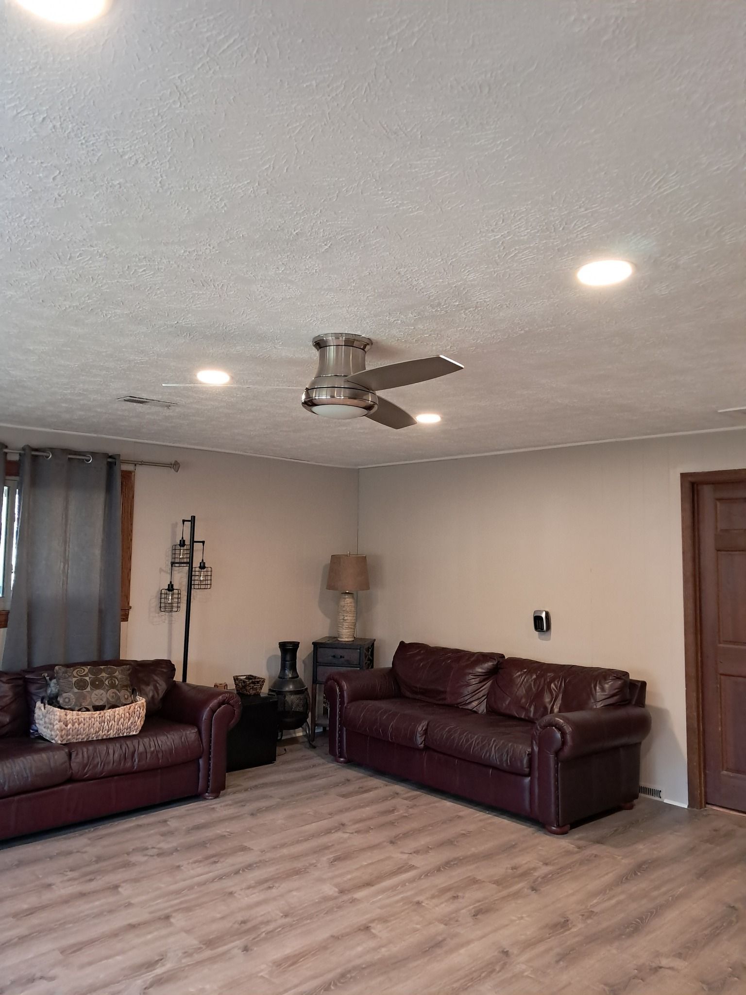 Living room with brown leather couches, wooden floor, and ceiling fan.