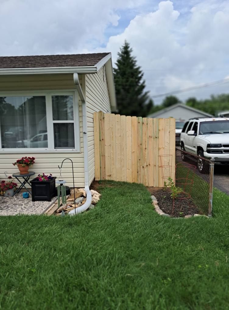 A light beige house with a new wooden fence on the side. A white SUV is parked nearby.