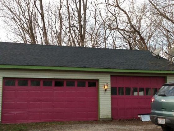 Red garage doors on a light yellow building, topped by a dark roof, trees in the background. Red garage doors on a light yellow building, topped by a dark roof, trees in the background.
