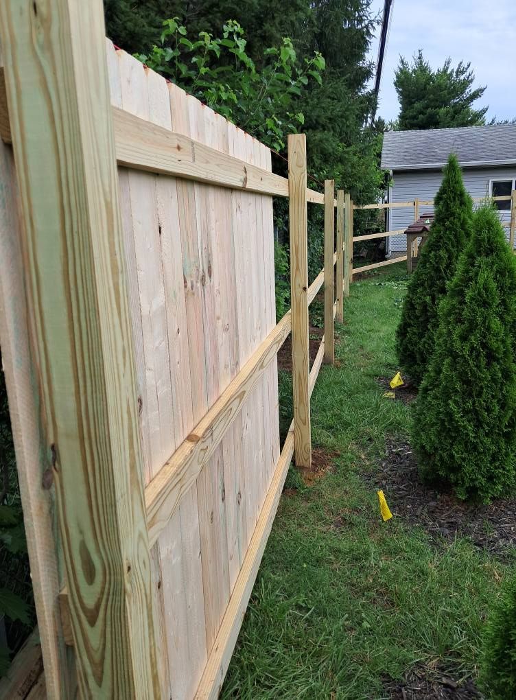 Wooden fence in backyard, adjacent to a smaller fence. Green grass, bushes, and a house visible.