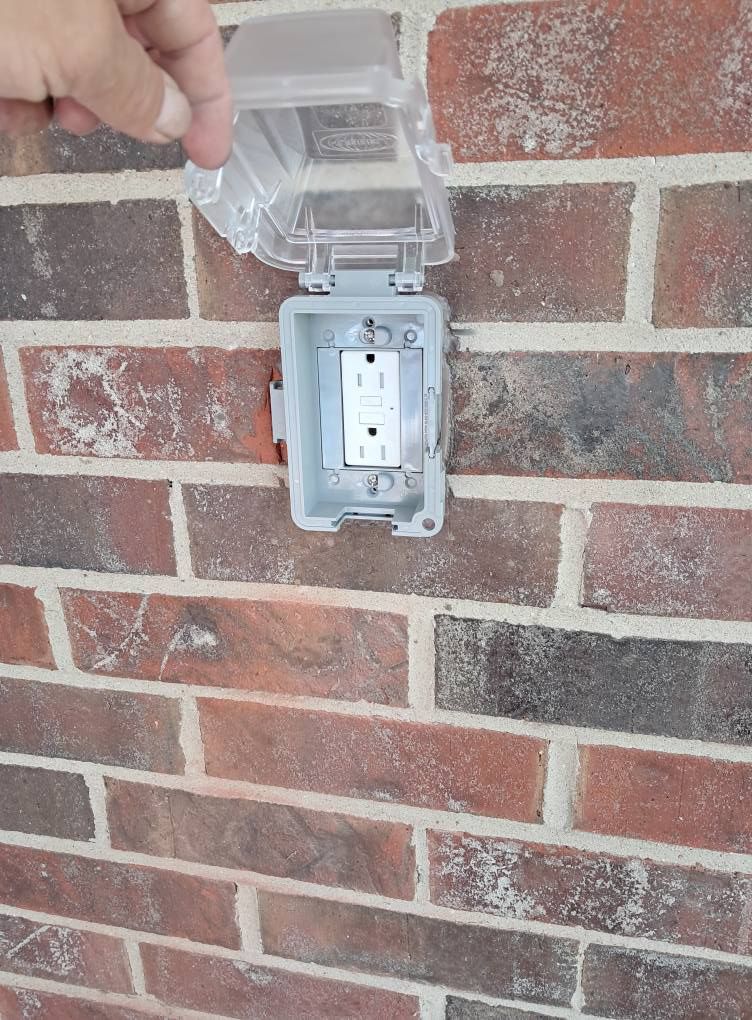 Outdoor electrical outlet with a clear cover on a red brick wall.