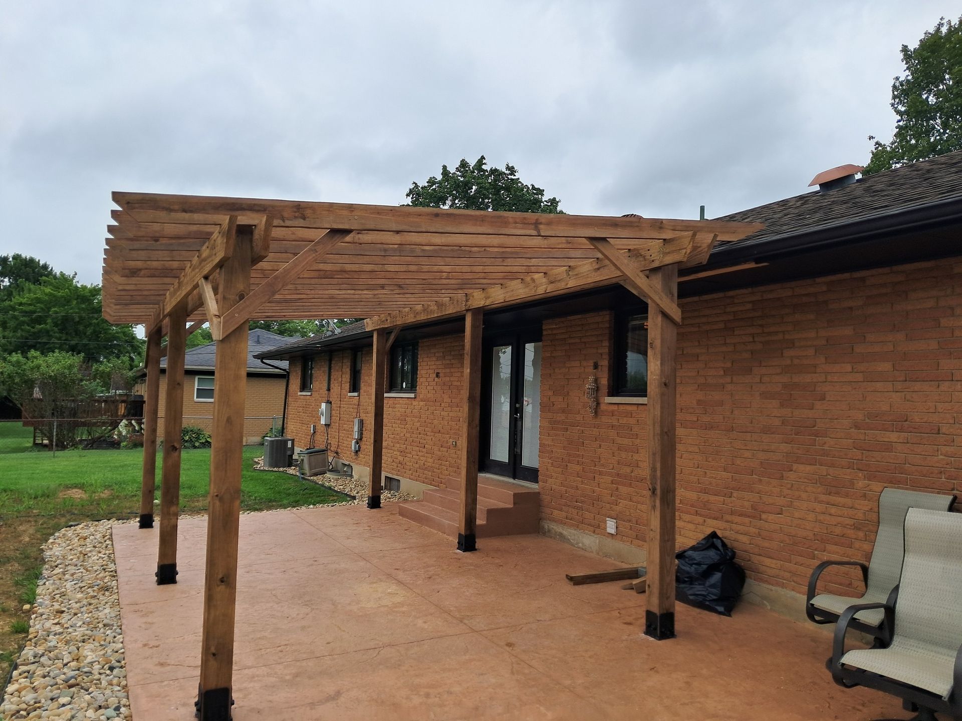 Wooden pergola over a concrete patio next to a brick house.